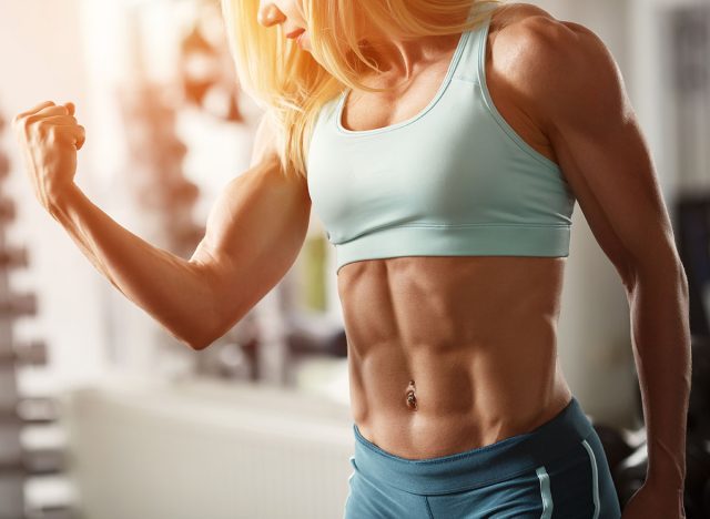 Brutal fitness blond with a muscular, straining biceps and abdominal muscles in the gym, part of the fitness body. Sports and fitness - concept of healthy lifestyle. Fitness woman in the gym.