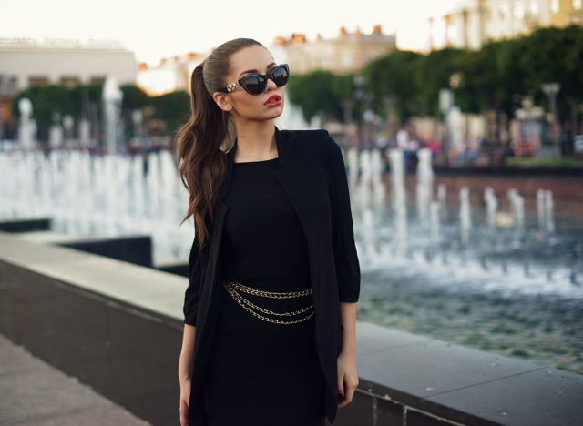 Young beautiful stylish girl walking and posing in short black dress in city near fountains. Outdoor summer portrait of young classy woman
