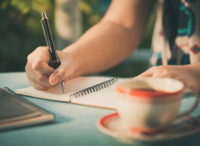 Woman hand writing journal on small notebook at outdoor area in cafe with morning scene and vintage filer effect