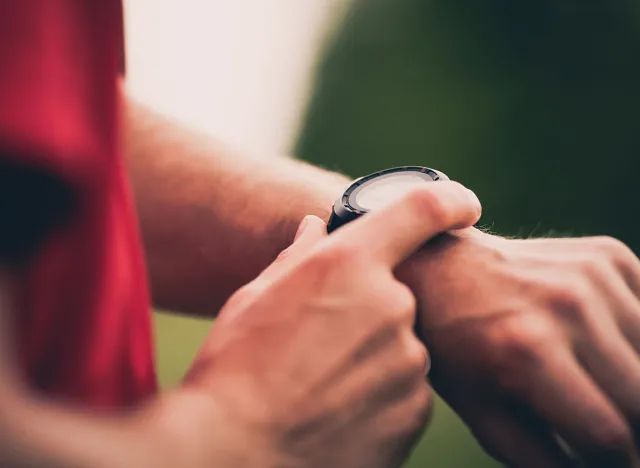 Runner using heart rate monitor training running, smartwatch checking performance or GPS. Man athlete looking at stopwatch. Healthy runner on running trail. Wearable technology for tracking activity.