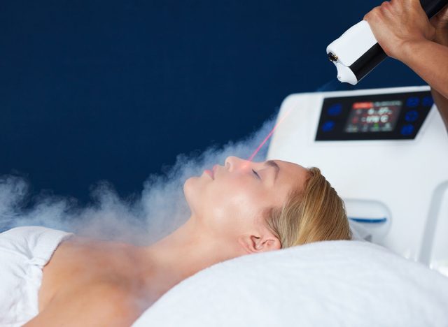 Beautiful young woman getting local cryotherapy therapy in cosmetology clinic. Beautician applying cold nitrogen vapors to the face of woman.