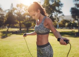 Portrait of fit young woman with jump rope in a park. Fitness female doing skipping workout outdoors on a sunny day.