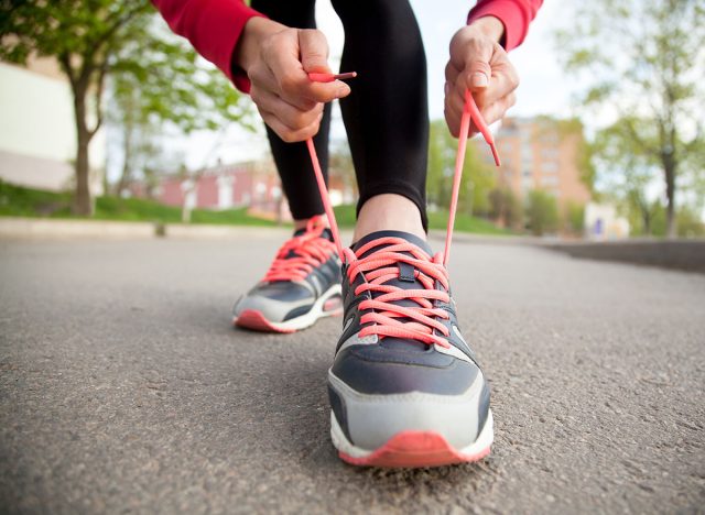 Sporty woman tying shoelace on running shoes before practice. Female athlete preparing for jogging outdoors. Runner getting ready for training. Sport active lifestyle concept. Close-up