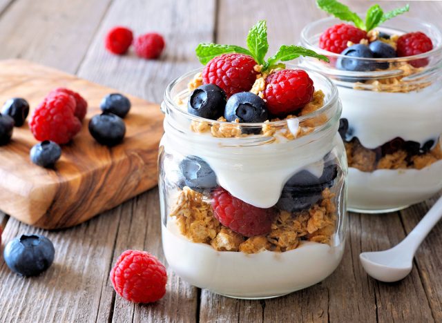 Blueberry and raspberry parfaits in mason jars, scene on a rustic wood background