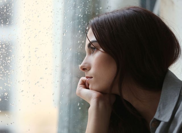 Depressed young woman near window at home, closeup