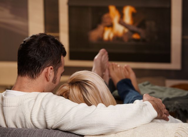 Couple sitting on sofa at home in front of fireplace, rear view.