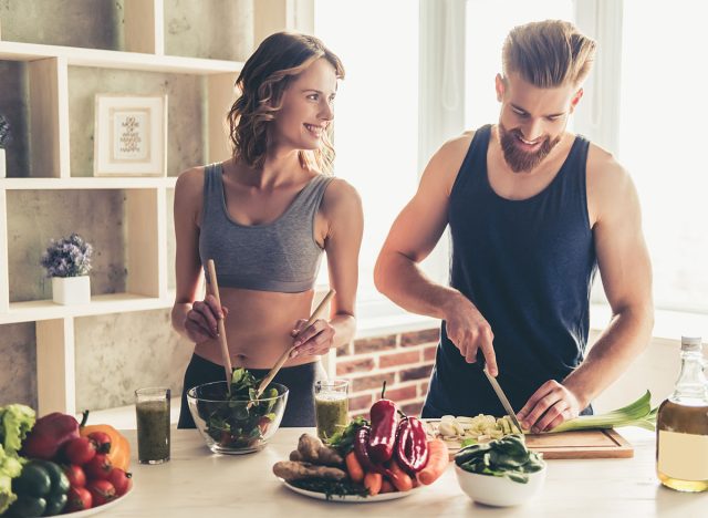 Beautiful young sports people are talking and smiling while cooking healthy food in kitchen at home