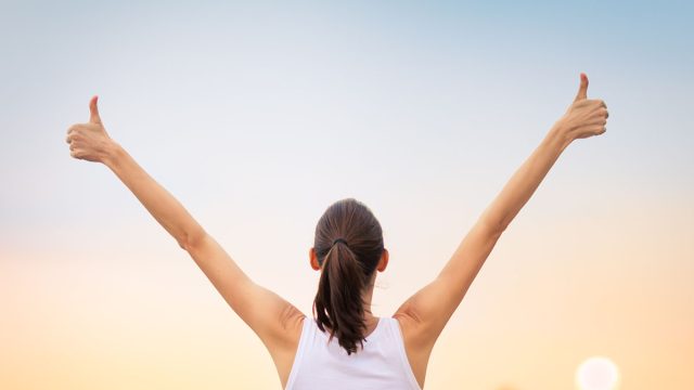 Winning, success and life goals concept. Young woman with arms in the air giving thumbs up.