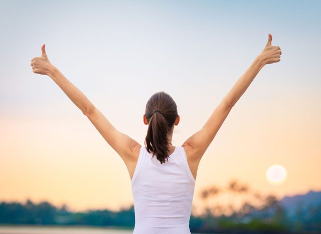 Winning, success and life goals concept. Young woman with arms in the air giving thumbs up.