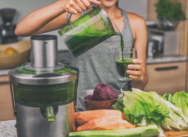 Woman juicing making green juice with juice machine in home kitchen. Healthy detox vegan diet with vegetable cold pressed extractor to extract nutrients for smoothie drink.