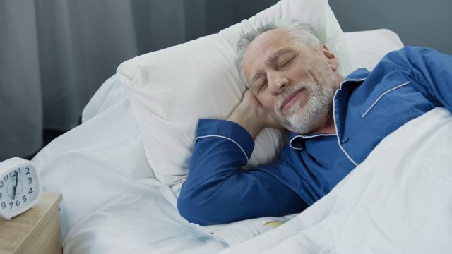 Senior man smiling while asleep in the morning, pleased pensioner lying in bed