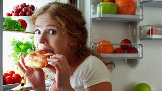 woman eats sweets at night to sneak in a refrigerator.