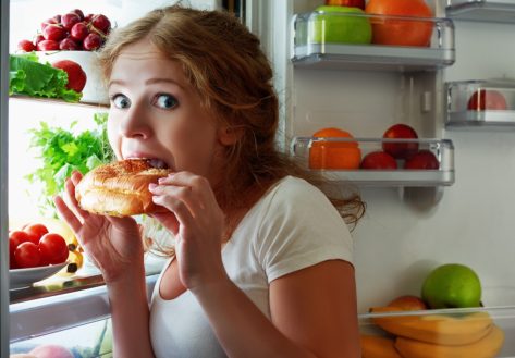 woman eats sweets at night to sneak in a refrigerator.