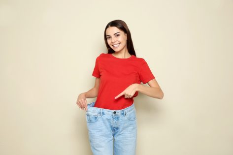 Slim woman in oversized jeans on color background.
