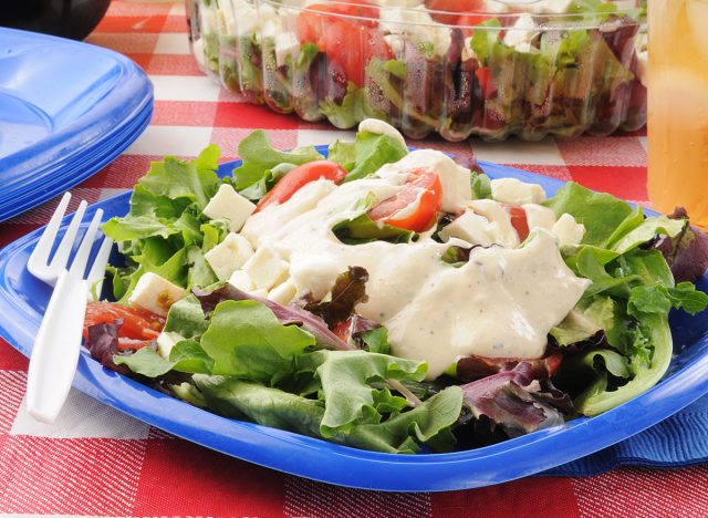 A plastic plate of salad with ranch dressing
