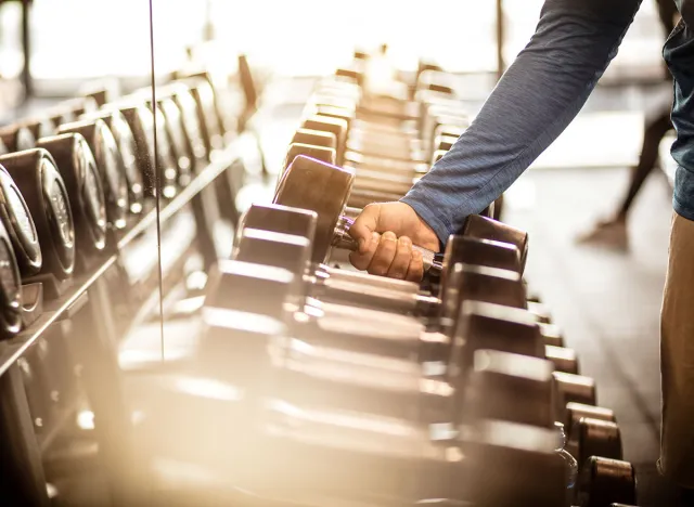 Muscular build sportsman taking weights from a rack in a gym. Focus is on hand. Close up.