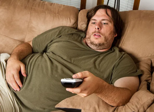 Overweight guy sitting on the couch with remote in hand trying to watch some TV.