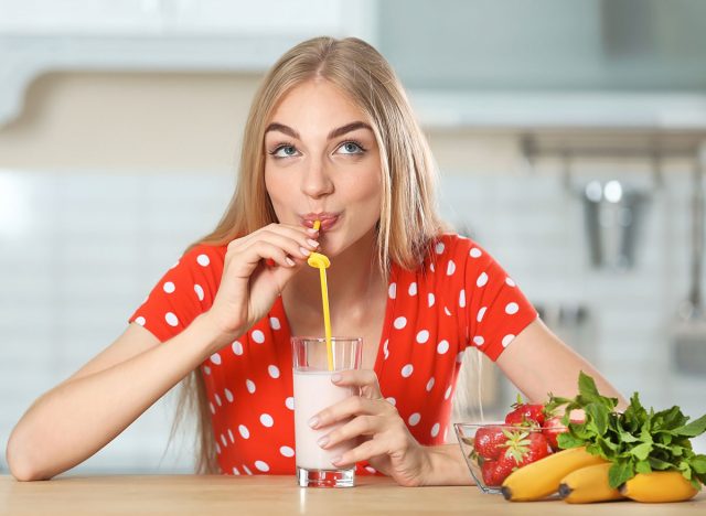 Young woman with glass of delicious milk shake in kitchen