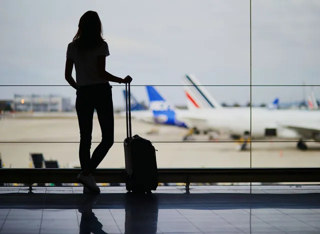 Silhouette of young woman in international airport, looking through the window at planes