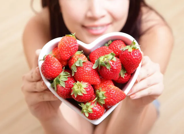 strawberry - Woman smiling with strawberry on wooden floor background, focus on fruit, asian beauty model