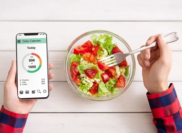 Smart eating and diet planning concept. Man eating vegetable salad and counting calories on mobile application, top view