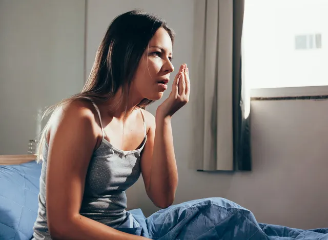 Woman sitting on her bed checking her breath in the morning. Concept of Bad Breath