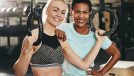 Two diverse young female friends in sportswear standing together by rings in a gym after a workout