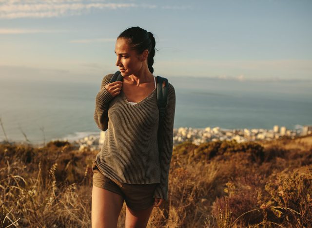 Young woman hiking up the hill and looking away. Female hiker walking on country trail.