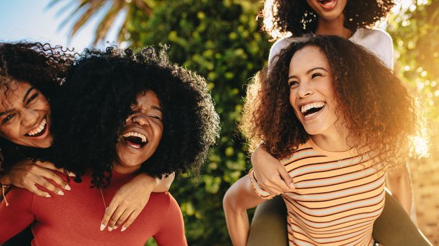 Cheerful female friends walking outdoors in city and having fun. Young women piggybacking their friends outdoors in the city.