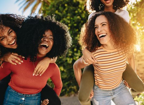 Cheerful female friends walking outdoors in city and having fun. Young women piggybacking their friends outdoors in the city.