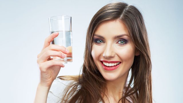 Casual style young woman posing on isolated studio background, hold water glass. Beautiful girl portrait. Female model poses.