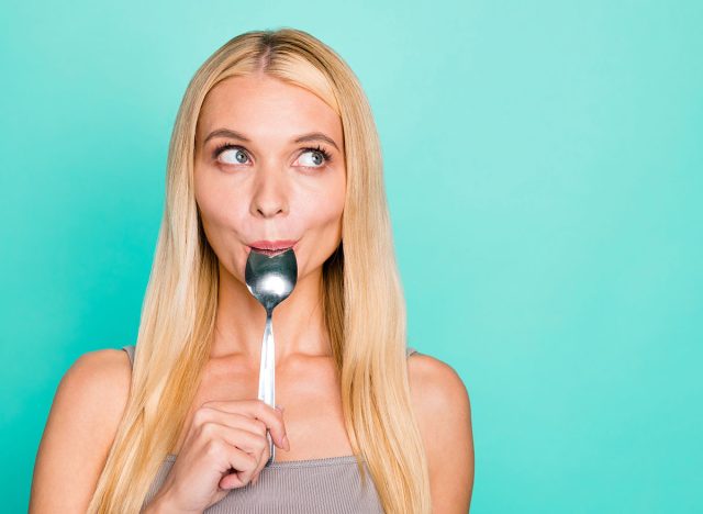 Close-up portrait of nice attractive lovely sweet girlish funny feminine funky cheerful straight-haired girl licking silver spoon lunch dinner isolated on bright vivid shine green turquoise background
