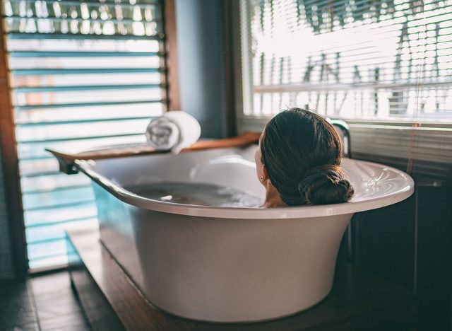 Bath taking woman relaxing in bathtub of hotel room at luxury overwater bungalow resort in Bora Bora, Tahiti.