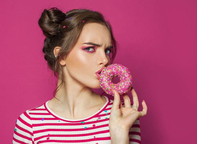 Diet concept. Doubting woman eating donut on vivid pink background