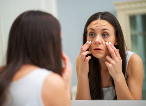 Tired woman looking at her eye bags in the bathroom.