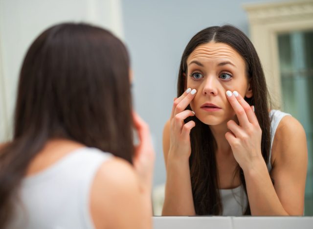 Tired woman looking at her eye bags in the bathroom.