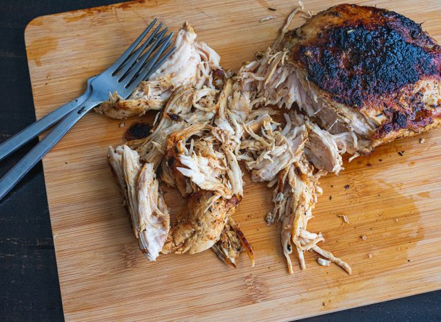 Shredding a Spiced Chicken Breast: Chicken breast cooked in Arabic spices being shredded with two forks on a bamboo cutting board