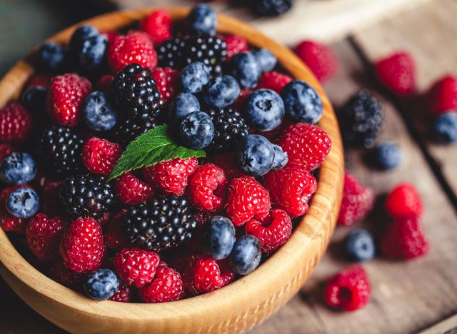 blueberries and raspberries, blackberry in a wooden bowl on old wood background