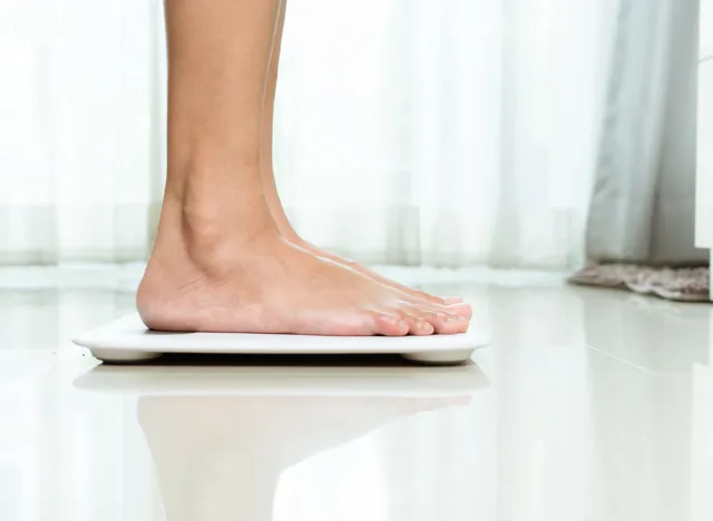 Overweight female is standing on white scales at home