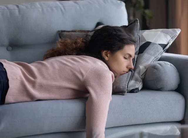 Exhausted young Caucasian woman lying on comfortable sofa in living room sleeping after hard-working day, tired millennial female fall asleep on couch at home, take nap or daydream, fatigue concept