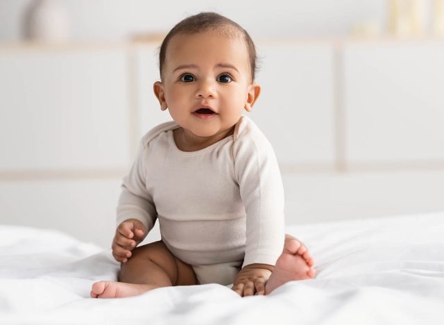 Cute little African American infant sitting on bed