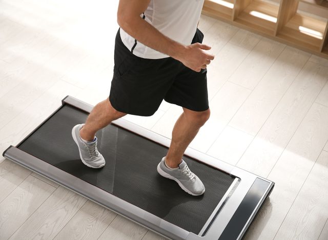 Sporty man training on walking treadmill at home, closeup