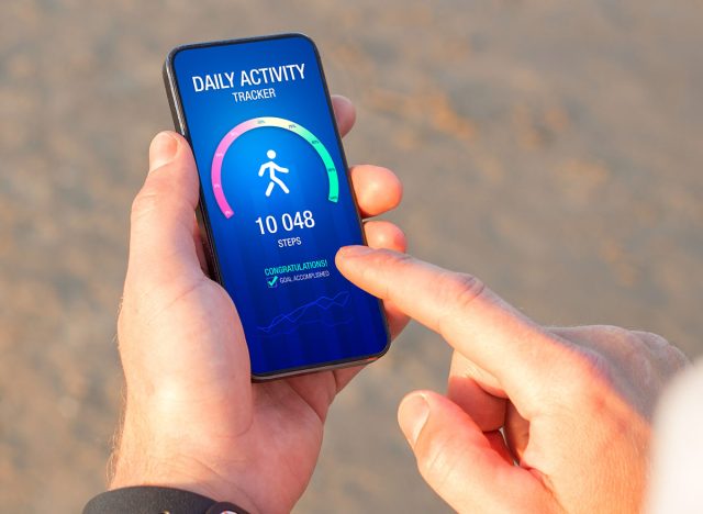 Man using daily activity tracking app on mobile phone showing 10 000 steps daily goal achievement