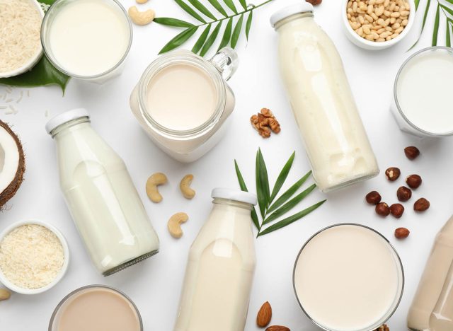 Different vegan milks and ingredients on white background, flat lay