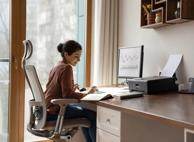 Concentrated young indian ethnicity woman sitting in comfortable adjustable ergonomic armchair with lumbar support, studying or working on computer in modern home office. distant workday concept.