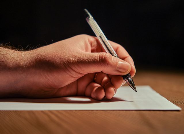 Man hand writes with a pen on a white sheet of paper, night dark background