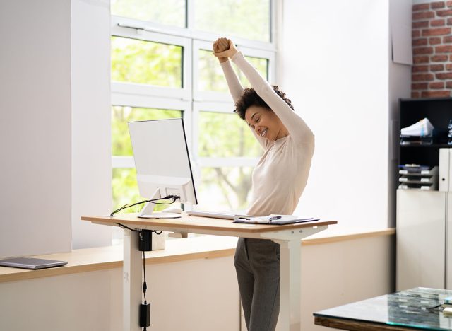 Worker Stretch Exercise At Stand Desk In Office