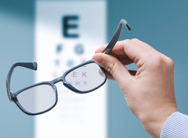 Professional optometrist holding glasses and eye chart in the background, eyesight and vision problems concept, copy space