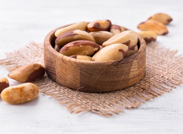 brazil nuts in the brown wooden plate on the piece of burlap on the white wooden table. catalog. brazilian nut