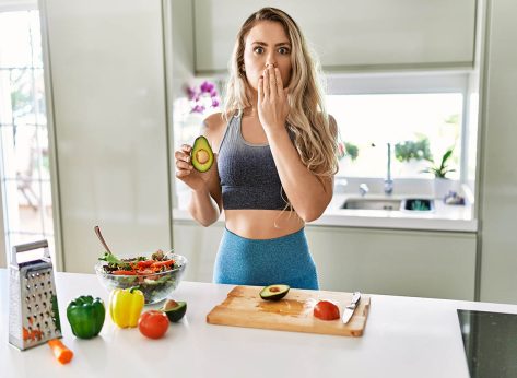 Young caucasian fitness woman wearing sportswear preparing healthy salad at the kitchen covering mouth with hand, shocked and afraid for mistake. surprised expression